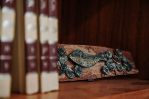 Fotografia de uma prateleira de livros com uma obra que remete a um peixe aplicado em uma madeira retangular.